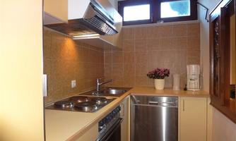 A modern kitchen with a bright interior and appliances. On the worktop, there is a flower vase, and there is a dishwasher.