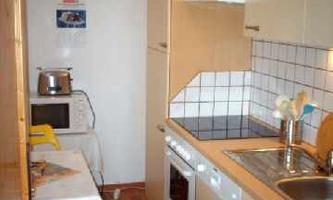 A small kitchen with modern appliances and wooden cladding. Kitchen utensils are placed on the countertop and there is a table with chairs.