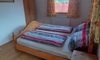 A cozy bedroom with a double bed and colorful bed covers. The room has large windows overlooking nature.