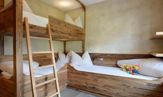 A cozy bedroom with a wooden bunk bed and a single bed. Plush toys are decorated on the bed.