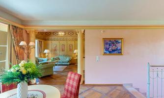A bright, inviting suite with a table and chairs as well as a cozy sofa in the background. Colored walls and decorative elements create a warm atmosphere.