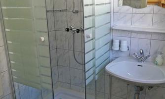 A modern bathroom with a glass shower and a sink. The walls are tiled with light tiles and there is a laundry basket in the corner.