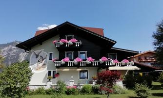 A charming house with blooming balconies and a beautiful garden. In the background, mountains and a clear blue sky are visible.