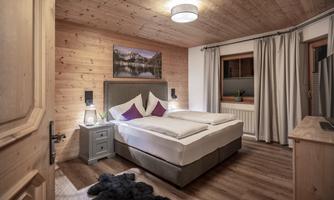 A cozy bedroom with a large bed and wooden paneling. The walls are light, and there is a beautiful picture of mountains above the bed.