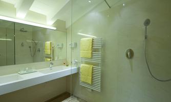 A modern bathroom with bright stone and large mirrors. Yellow towels and a shower are clearly visible.