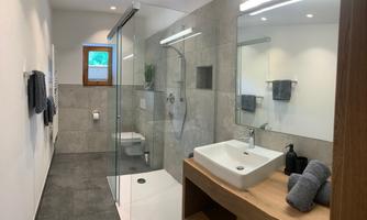 A modern bathroom with a glass shower and a wooden washbasin. The walls are in neutral colors, and there are appealing towels and plants.