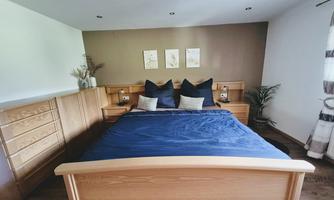 A cozy bedroom with a large bed and wooden furniture. The walls are kept neutral, and there are some decorations as well as plants.