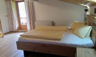 A cozy bedroom with a double bed and bright ceilings. Large windows provide plenty of daylight and a view outside.