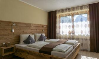 A modern bedroom with a wooden frame bed and a cozy design. Large windows let in plenty of natural light and offer a view outside.