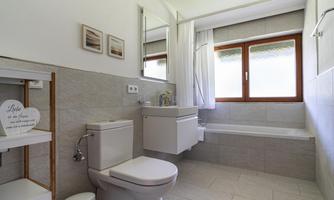 A modern bathroom with a bathtub and a window that lets in daylight. White walls and light tiles create a friendly atmosphere.