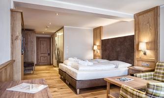 A cozy hotel room with a double bed and wooden interior. The warm lighting and comfortable armchairs create an inviting atmosphere.