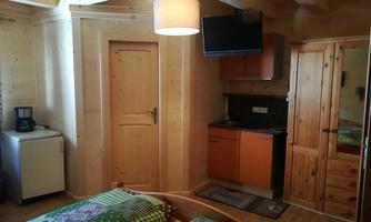 A cozy room with wooden paneling and a television. There is a small kitchenette and a double bed with colorful bedding.