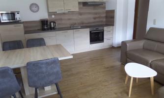 A modern kitchen with wooden furniture and a dining table. In the living area, there is a cozy sofa and a small table.