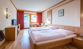 A cozy room with two beds and wooden interiors. Large windows offer a view of the outdoor area.