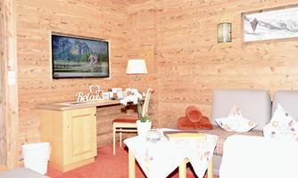 A cozy living area with wooden walls and a television. A table with a tablecloth and a plant creates an inviting atmosphere.