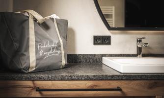 A bag is standing on a wood and granite surface next to a sink. The bag is dark gray with an inscription.