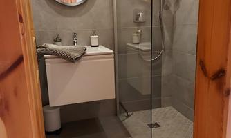 A modern bathroom with a glass shower cabin and a wall-mounted sink. The space is decorated in neutral shades of gray and features a round mirror.