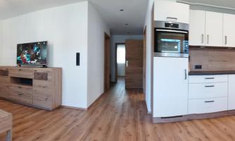 A modern living kitchen with an open space concept. The furniture is made of wood and the floor is wood-colored, with a cozy sofa and a dining table.