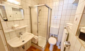 A bright bathroom with tiles and a wooden ceiling. It includes a shower, a sink, and a toilet.