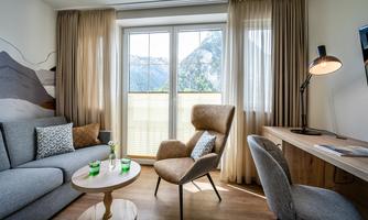 A modern living room with a cozy sofa and an elegant armchair. Large windows offer a view of the mountains and let in plenty of daylight.