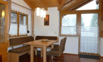 A cozy dining area with a wooden table and comfortable chairs. Large windows provide plenty of light and a pleasant atmosphere.