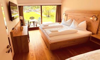 A cozy hotel room with two beds and wooden decor. Large windows offer a view of greenery.