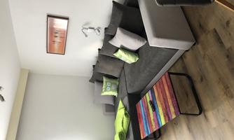 A modern living room with a gray couch and a colorful table. On the couch, there are green pillows and a blanket.