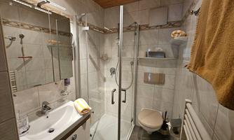 A modern bathroom with a shower and a sink. Light gray tiles and a wooden ceiling create a cozy atmosphere.