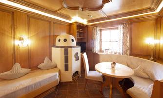 A cozy room with wooden walls and a small seating area. A round table and a stove create a warm atmosphere.