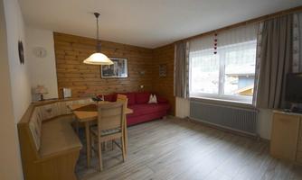 A bright living room with a cozy red couch and a dining area. Large windows provide plenty of daylight.