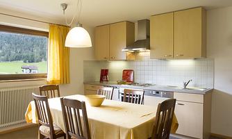 A cozy kitchen with a large table and wooden chairs. The windows offer a view of the green landscape.
