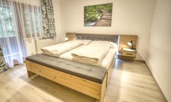 A modern bedroom with a large double bed and wooden details. On the wall hangs a picture of a wooden footbridge in nature.