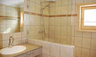 A modern bathroom with tiles and a shower over the bathtub. There is a sink with an elegant faucet and a window for natural light.