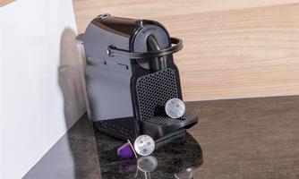 A compact coffee machine stands on a shiny countertop. Next to the machine are two coffee capsules.