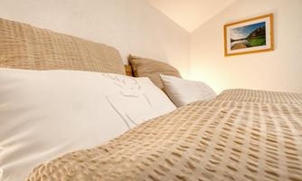 A cozy bedroom with a large bed and neutral bed linen colors. A picture of a landscape hangs on the wall.