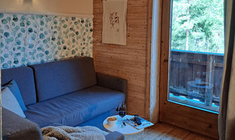 A cozy living area with a gray sofa and a small table. With access to the balcony and a lot of greenery to see.