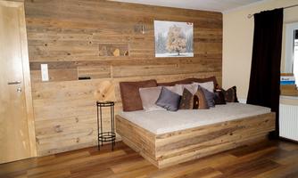 A modern living room with a wooden wall and a cozy sofa bed. Cushions in neutral colors give the room an inviting atmosphere.