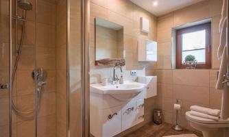 A modern bathroom with a shower and a sink. The walls are in neutral tones, and a window provides plenty of natural light.
