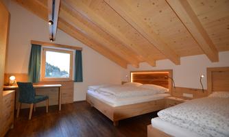 A cozy room with a wooden ceiling and two beds. There is a desk and a window overlooking the surrounding landscape.