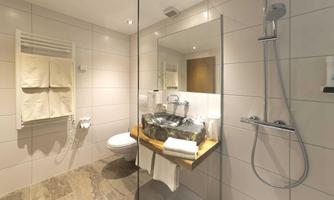 A modern bathroom with elegant design. It features a shower, a stone sink, and fluffy towels.