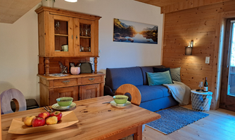 A cozy living space with a wooden table and a blue couch. On the table, there are apples, and a picturesque landscape adorns the wall.