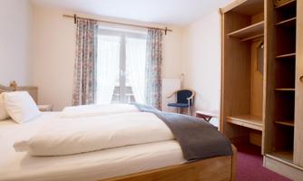 A simple bedroom with two single beds and a wardrobe. The large windows let in plenty of daylight.