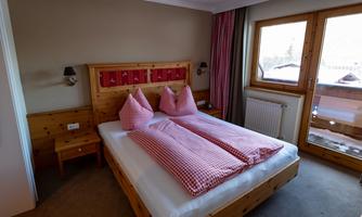 A cozy bedroom with a double bed and checkered cushions. Large windows offer a view outside.