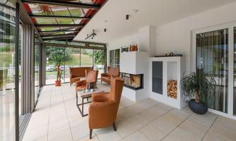A bright conservatory with modern furniture and large windows. The cozy atmosphere is complemented by a fireplace and plants.