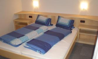 A simple bedroom with a large bed and blue bedding. On the walls, there are two bedside lamps and two nightstands.