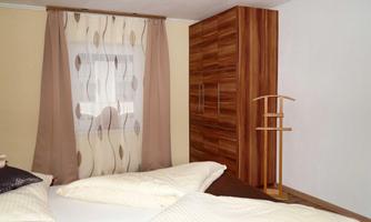 A cozy bedroom with a double bed and a wooden wardrobe. The room is decorated with curtains in soft colors.