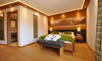 A modern bedroom with a large bed and wooden details. The walls are light, and there is soft lighting for a cozy atmosphere.