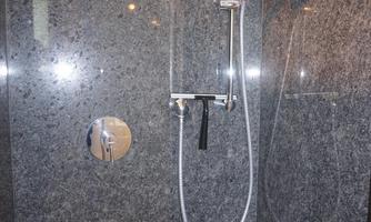 A modern shower with gray stone tiles. The shower fixture is made of metal and elegantly designed.