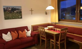 A cozy living room with a red sofa and a dining table. Large windows provide light and offer a view outside.