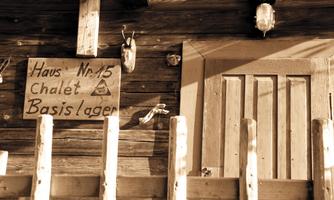 A rustic wooden house with a sign indicating "House No. 15." The facade is adorned with traditional fencing and a rural-style door.